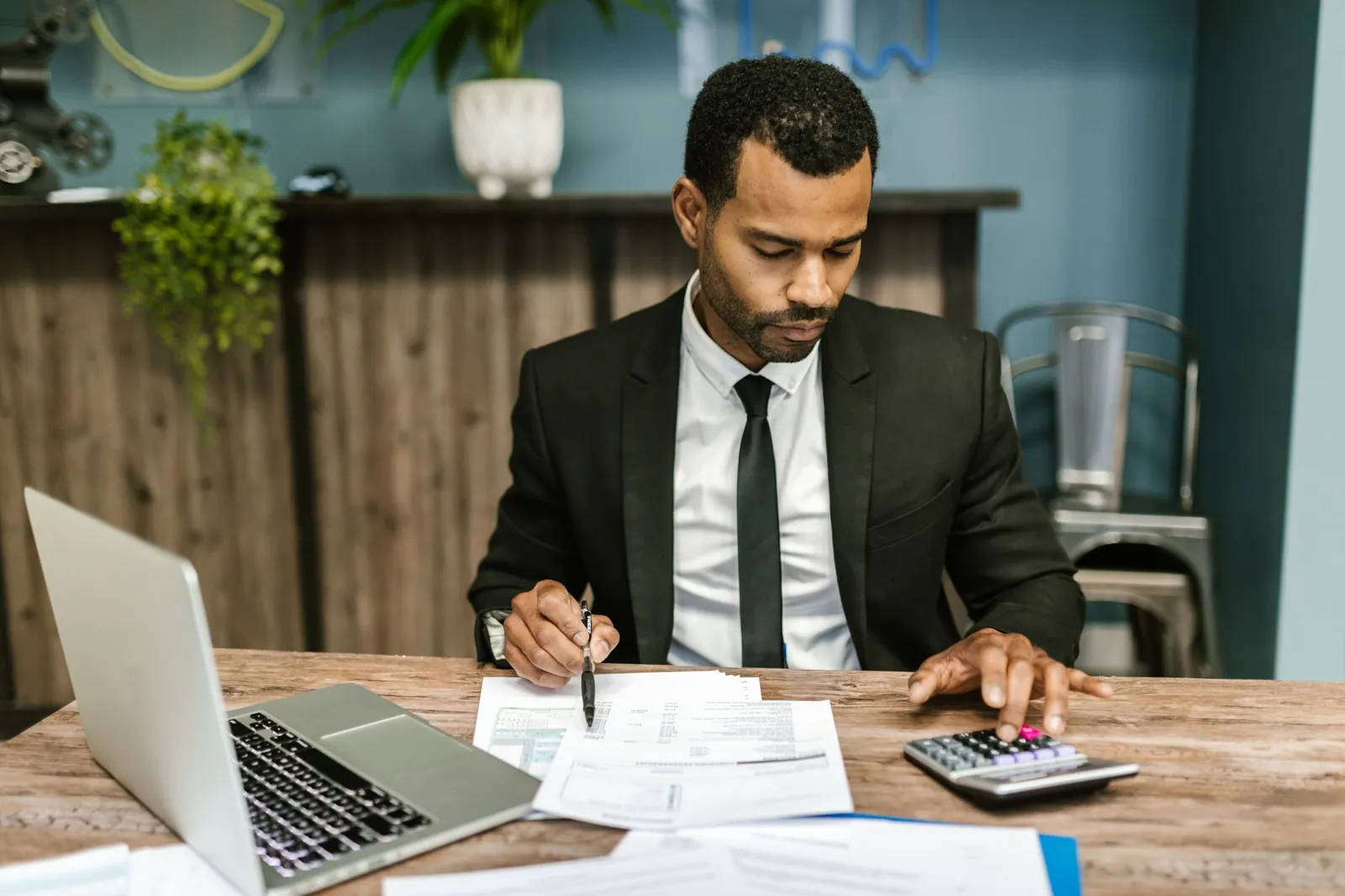 Accountant in a suit working through financial documents with a calculator and laptop
